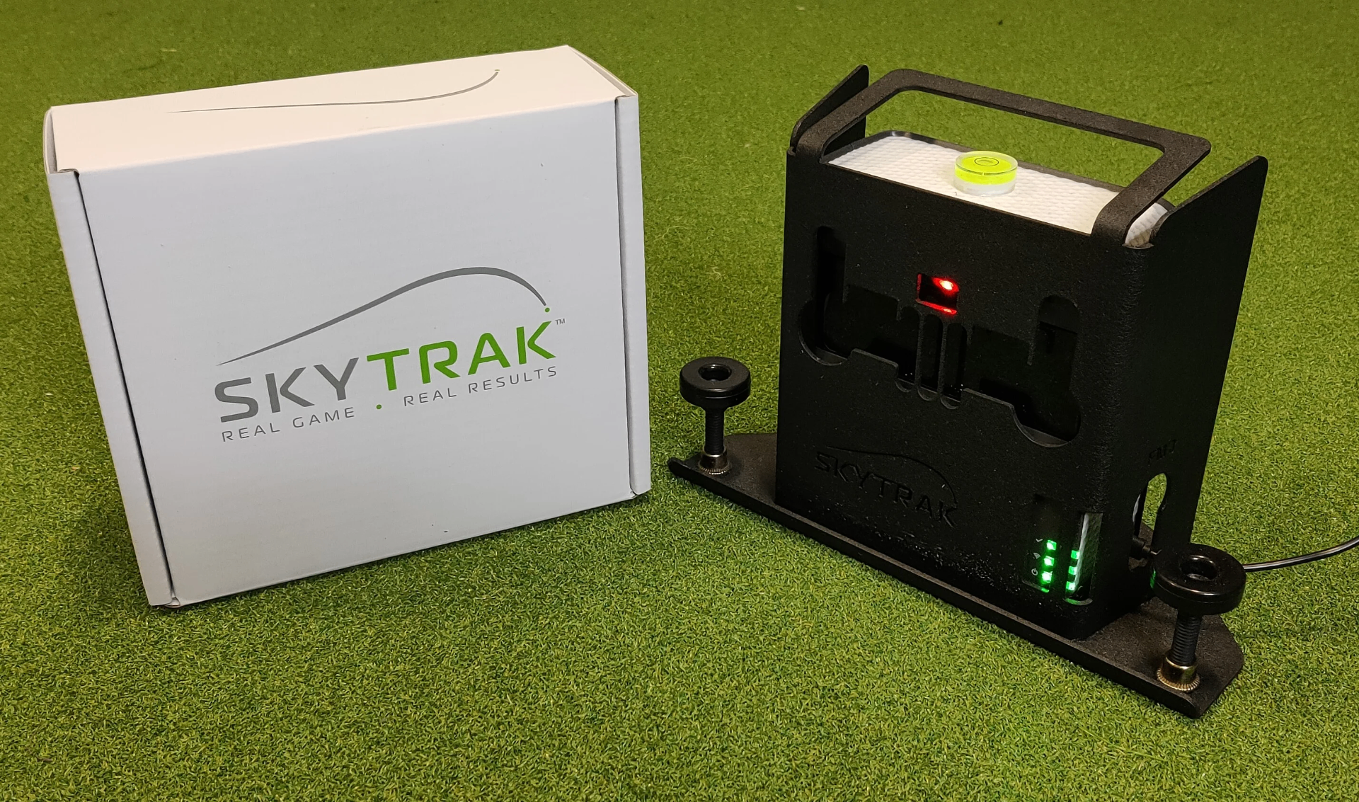 SkyTrak launch monitor on artificial turf in front of a projector screen